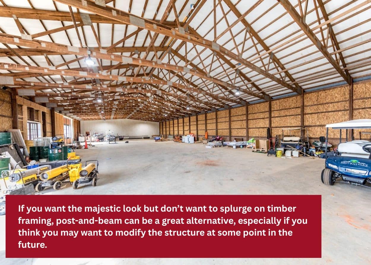 Wide interior of a post-and-beam barn with open trusses and concrete floor. Caption: If you want the majestic look but don’t want to splurge on timber framing, post-and-beam can be a great alternative, especially if you think you may want to modify the structure at some point in the future.